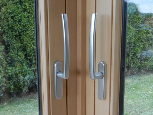 Zwei silberne Türgriffe an einem beige gefärbten Fenster.
