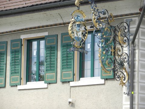 Fenster mit grünen Läden und dekorativem Schilderausleger an einer Fassade.